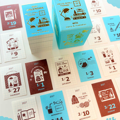 A stack of illustrated calendar cards and a matching calendar box displayed on a white background. The cards and box feature retro-style drawings and text in light blue, cream, and reddish brown, with the year 2027 prominently printed on the top pieces.